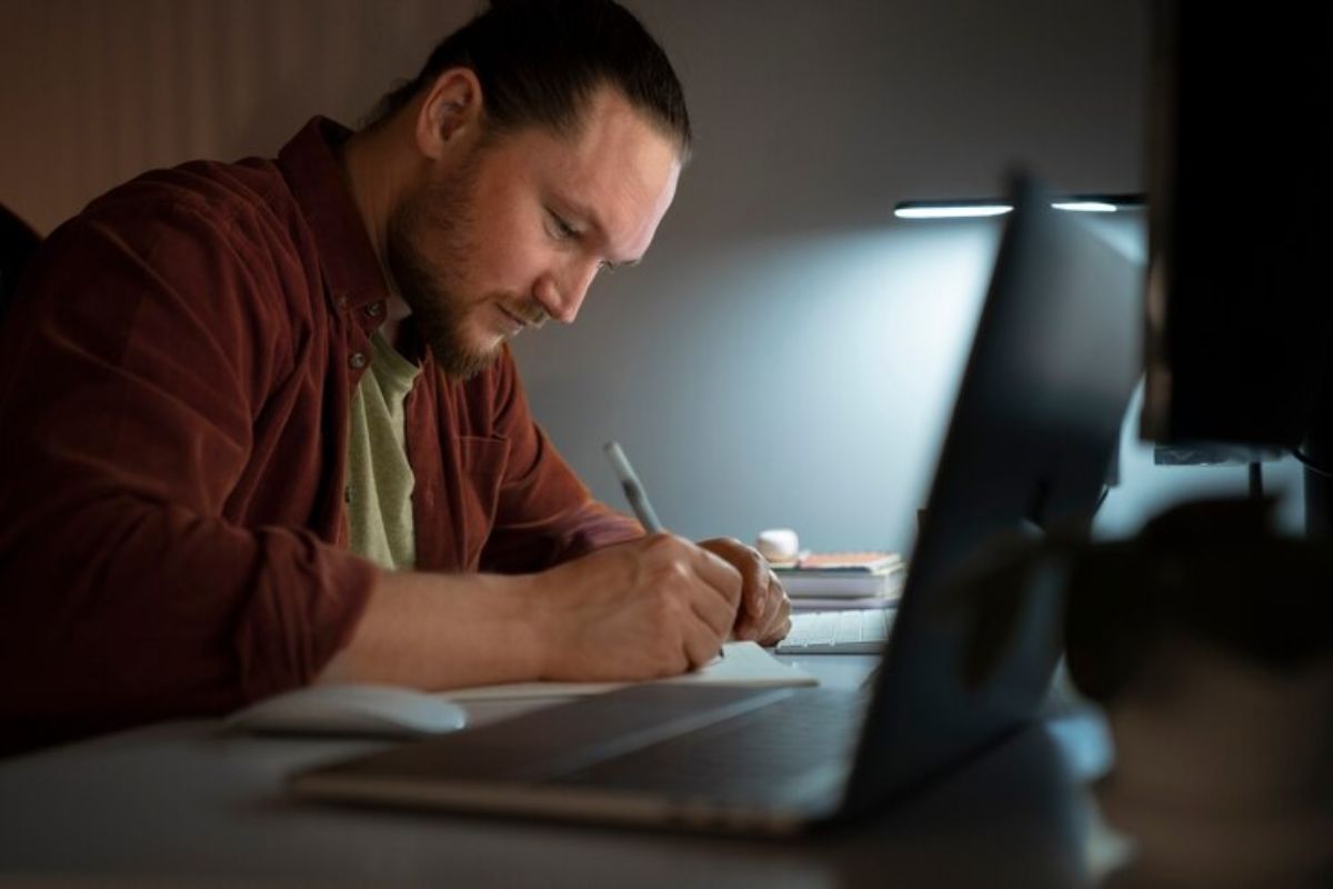 Um jovem em frente ao notebook confere o edital do vestibular UFPA 2025. Ele faz anotações em seu caderno com uma caneta