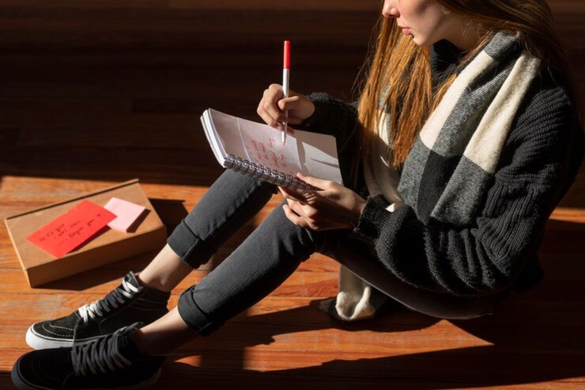 Uma estudante sentada no chão responde questões em seu caderno. Ela se prepara para o Vestibular Unifesp 2025