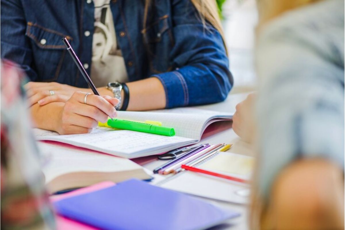 Imagem de estudantes em uma sala de aula de preparação para o Enem 2025. É possível ver alguns materiais na mesa 