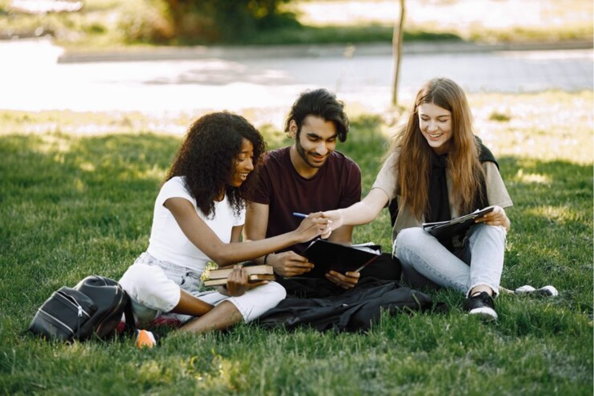 Três alunos sentados no jardim da escola conversam acerca do Vestibular ETEC 2025