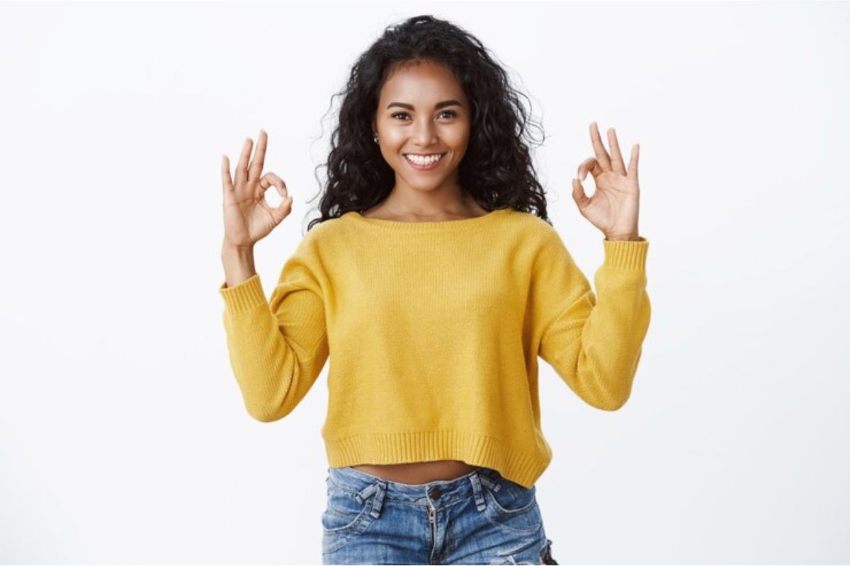 Uma menina de blusa amarela na frente de um fundo branco, ela pousa para a foto fazendo um mudra 