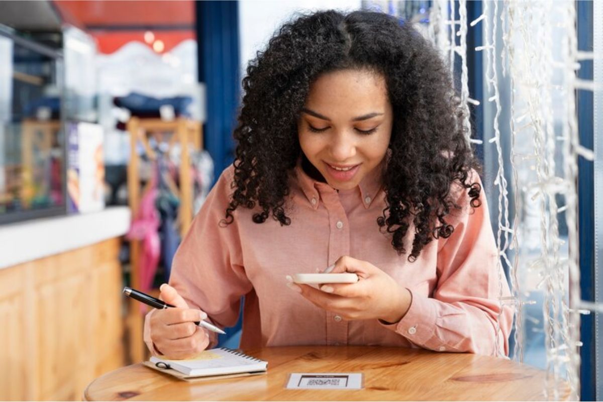 Uma menina olha para seu celular e faz anotações em seu caderno sobre o Vestibular Univesp 2025