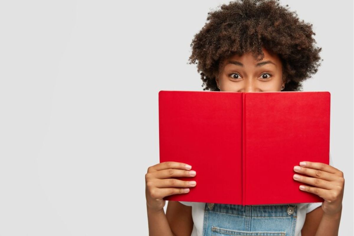 Uma menina com um caderno vermelho aberto na altura da boca