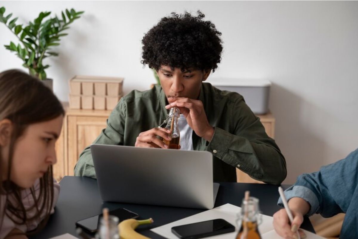 Um trio de alunos na mesa, um deles, está no notebook fazendo a inscrição no vestibular URCA 2025. Ele bebe refrigerante pelo canudo