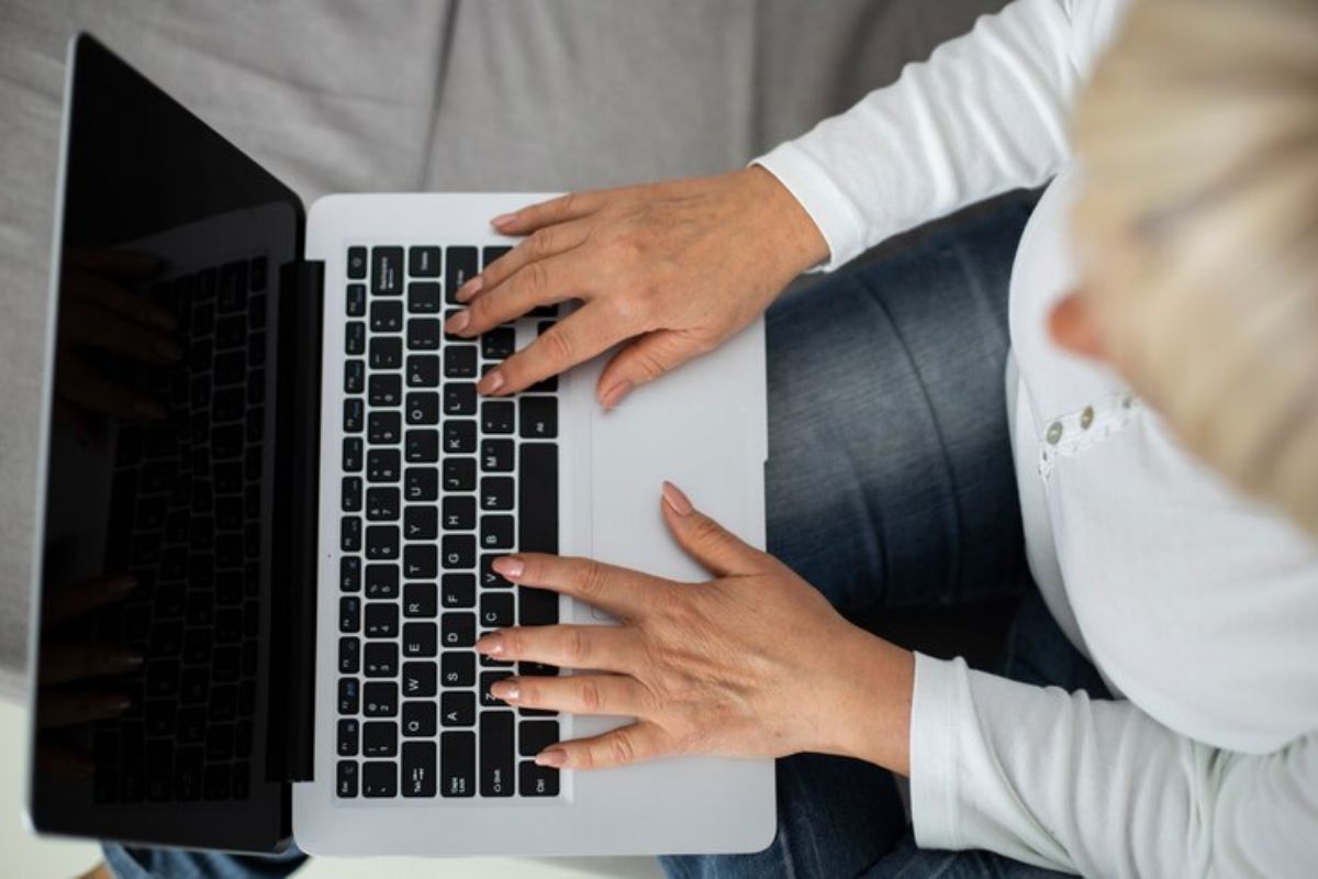 Imagem de uma pessoa vista de cima com o notebook no colo, enquanto se inscreve no Vestibular UNEB 2025