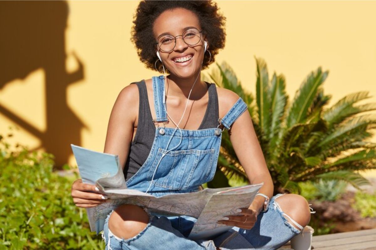 Uma menina sentada na mureta do campus enquanto abre uma revista e sorri para a foto