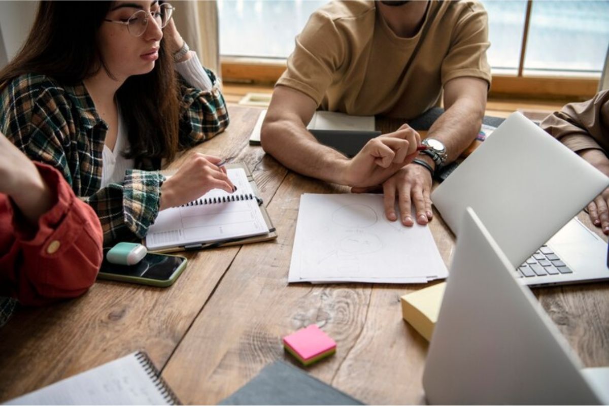 Um grupo de estudantes ao redor de uma mesa. Cada um consulta as informações em seus materiais de estudo