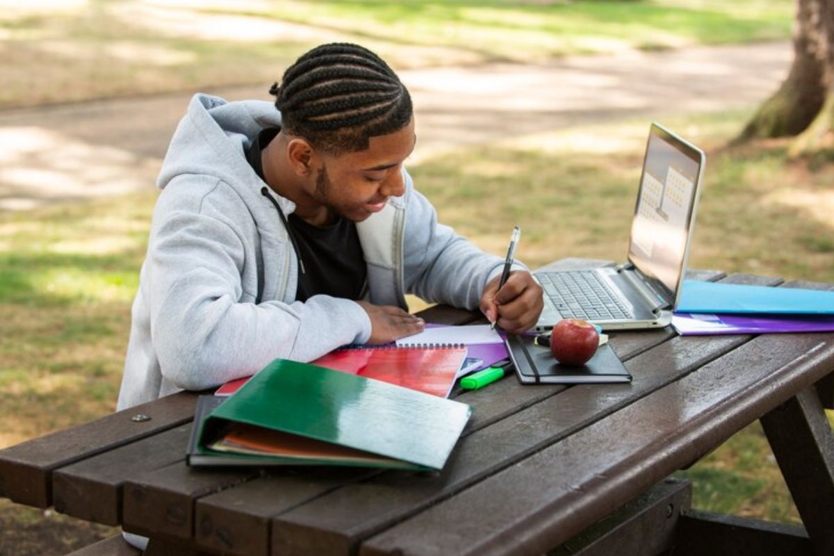 um aluno no grama da escola estuda em uma mesa. Ele usa seu notebook para ver o vestibular de medicina fácil de passar 2025