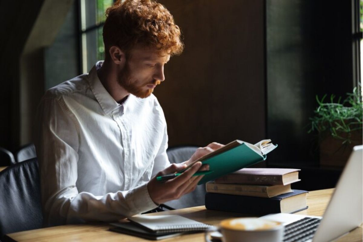 Um estudante em seu quarto lê um livro aberto, ele estuda para o vestibular UECE 2025