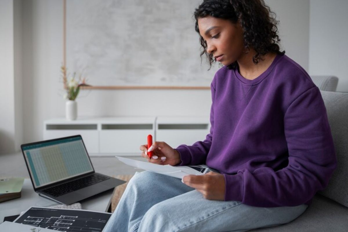 Uma menina sentada em frente ao seu notebook com uma folha e caneta na mão. Ela anota as informações sobre o Vestibular UFBA 2025