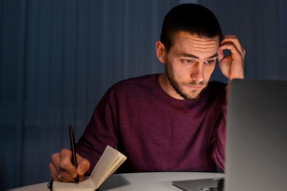 Um jovem em frente ao notebook confere o edital do vestibular UFPA 2025. Ele faz anotações em seu diário com uma caneta