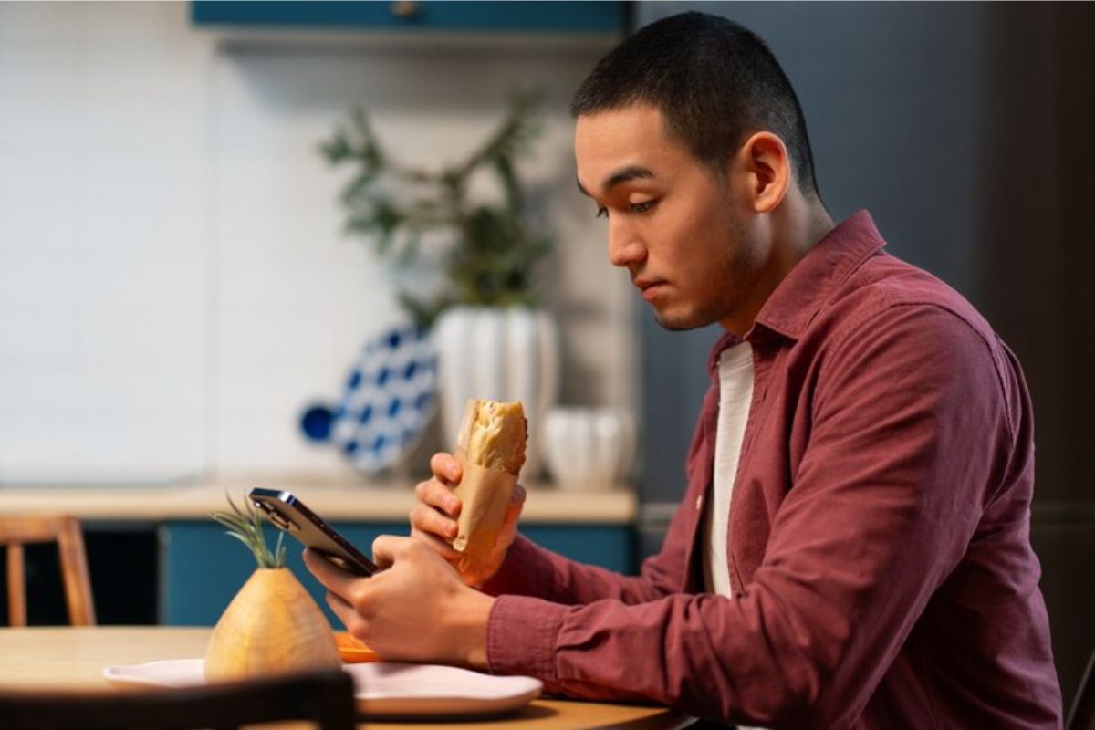 Um jovem comendo um salgado e vendo os detalhes do vestibular URCA 2025 em um celular