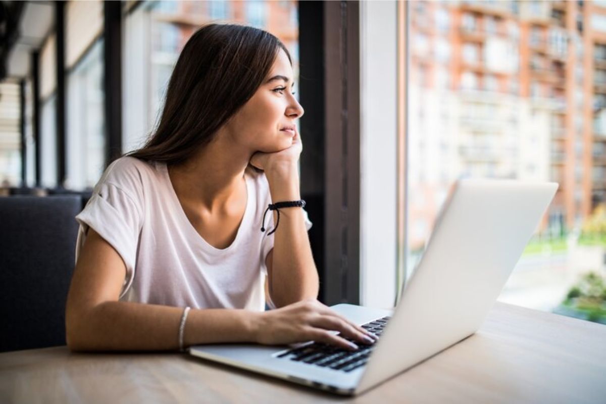 Uma estudante em frente ao seu notebook conferindo o Edital Fies 2025. Ela olha para a janela enquanto digita