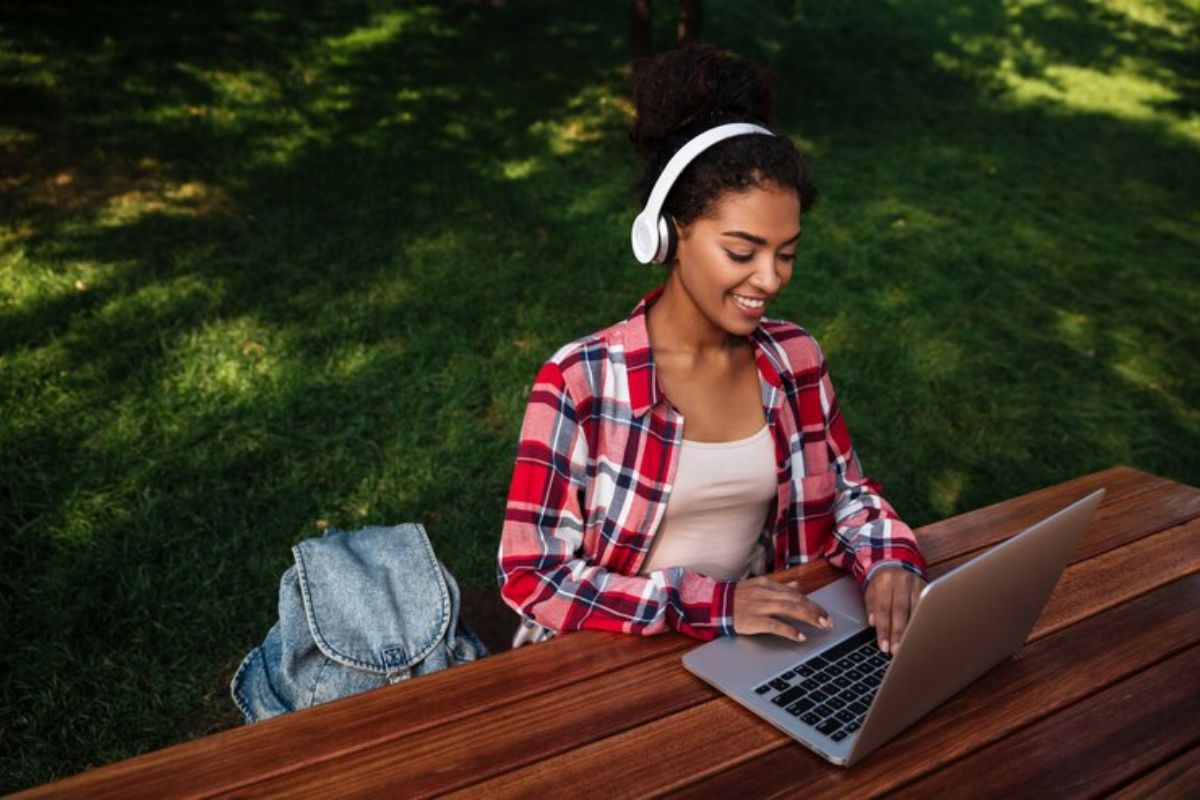 Uma aluna no jardim da escola. Ela está sentada em uma mesa acessando alguns pré-vestibulares online 2025 em seu notebook