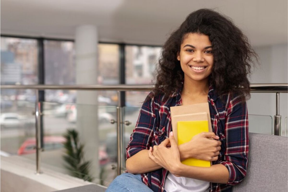 Uma estudante segurando um caderno de capa amarela e sorrindo