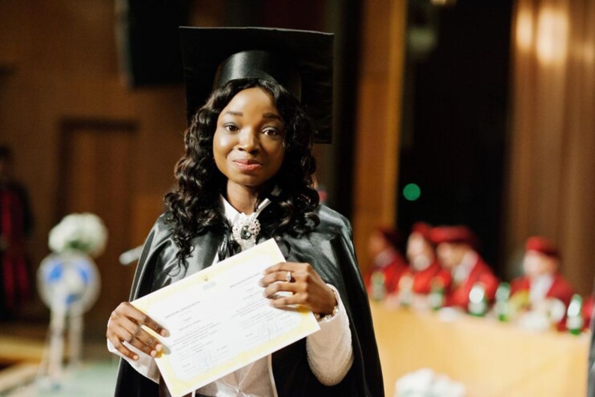 Uma estudante com roupa de formanda. Ela segura a folha de seu diploma e deseja passar no Vestibular UEPG 2025