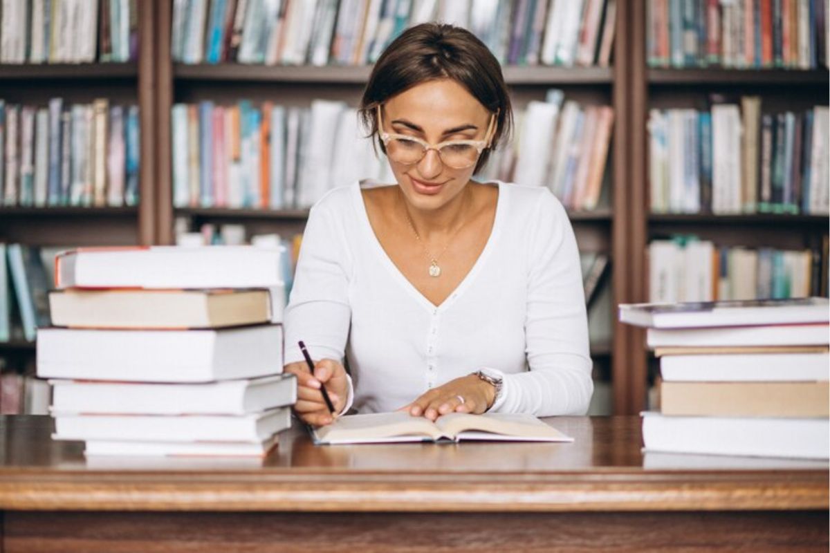 Uma estudante na biblioteca lendo um livro enquanto se prepara para o Vestibular UESB 2025