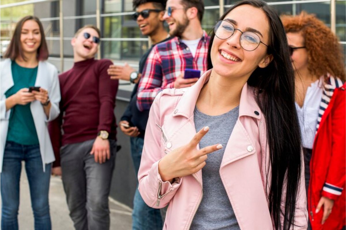 Um grupo de estudantes presentes para fazer o Vestibular UNIP 2025. Uma aluna mais à frente faz um sinal com dois dedos (V) e sorri