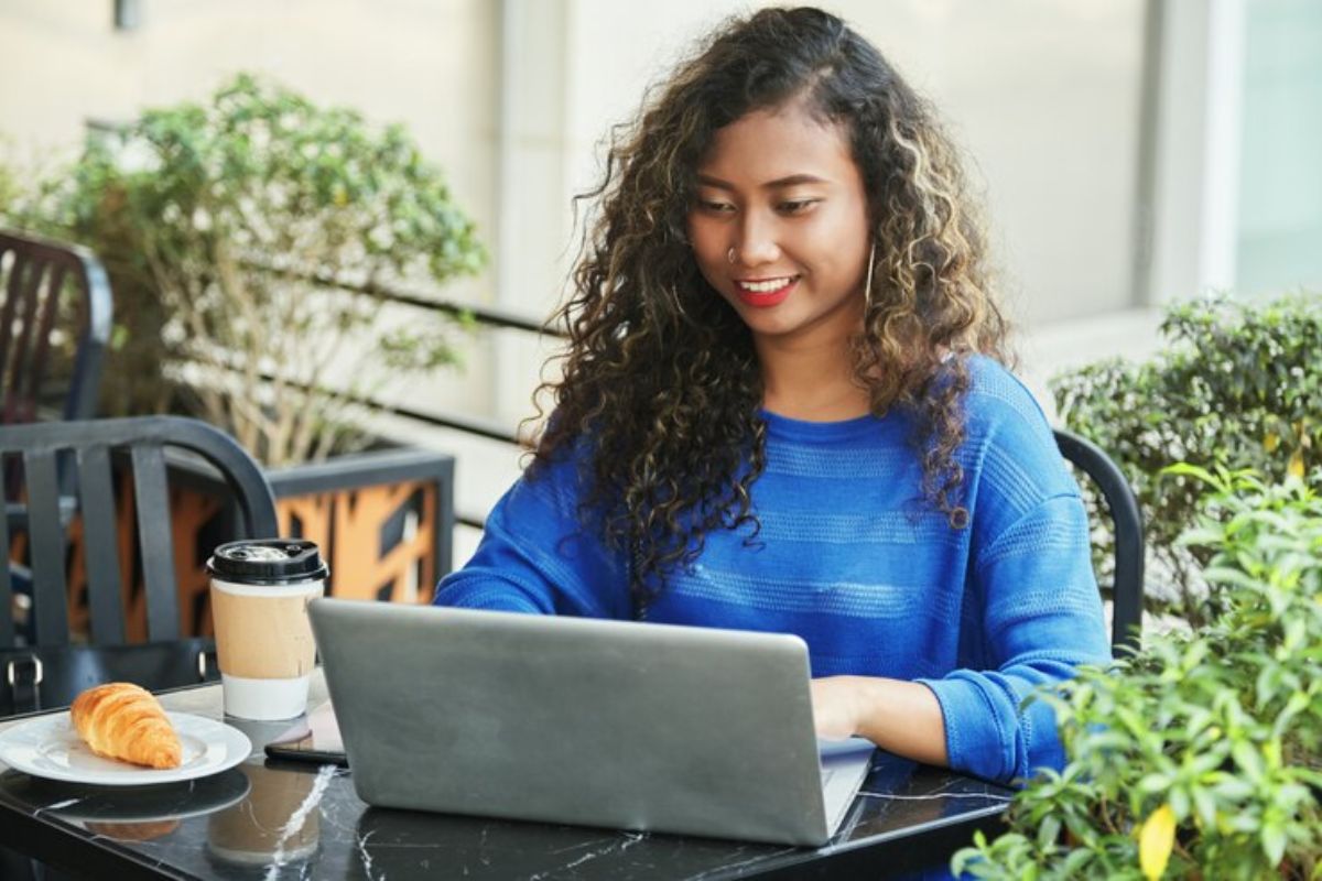 Uma aluna de azul sentada na mesa com seu notebook, onde ela faz o pedido da Dilatação FIES 2025