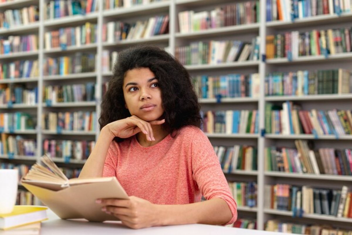 Uma estudante na biblioteca lê um livro e se prepara para o FIES UniFG 2025