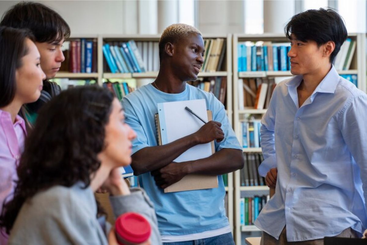 um grupo de quatro estudantes conversa dentro da biblioteca 