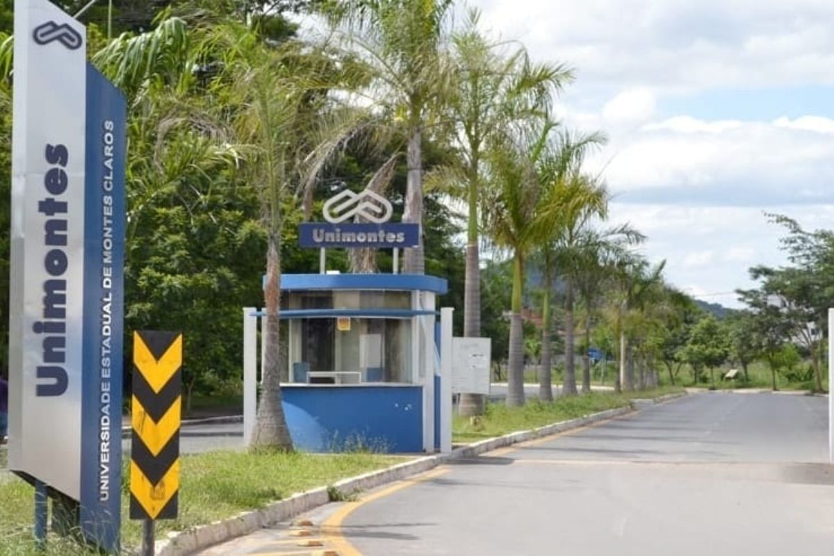 Foto da entrada da Unimontes. À esquerda há um letreiro vertical com o nome da universidade. Um pouco à frente é possível ver um posto de guarda 