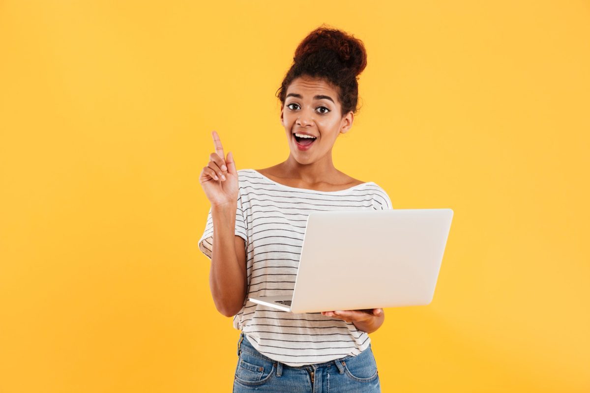 Jovem estudante com expressão animada com um notebook aberto na mão 