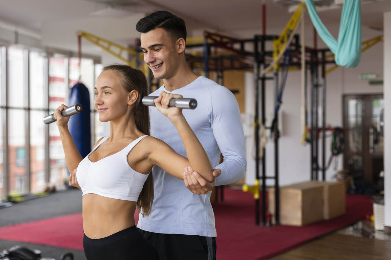 Personal trainner orienta exercícios de sua aluna na academia 