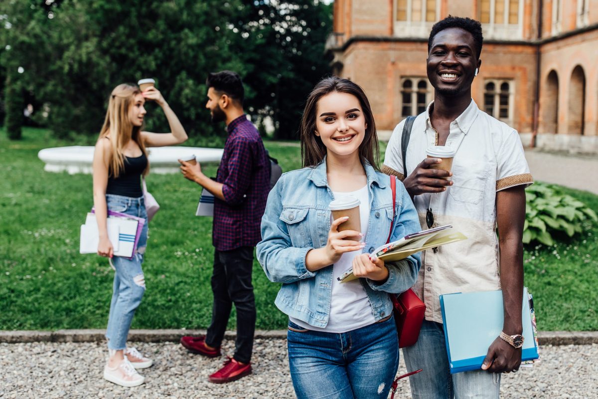 Estudantes com cadernos e copos de café nas mãos no campus da universidade