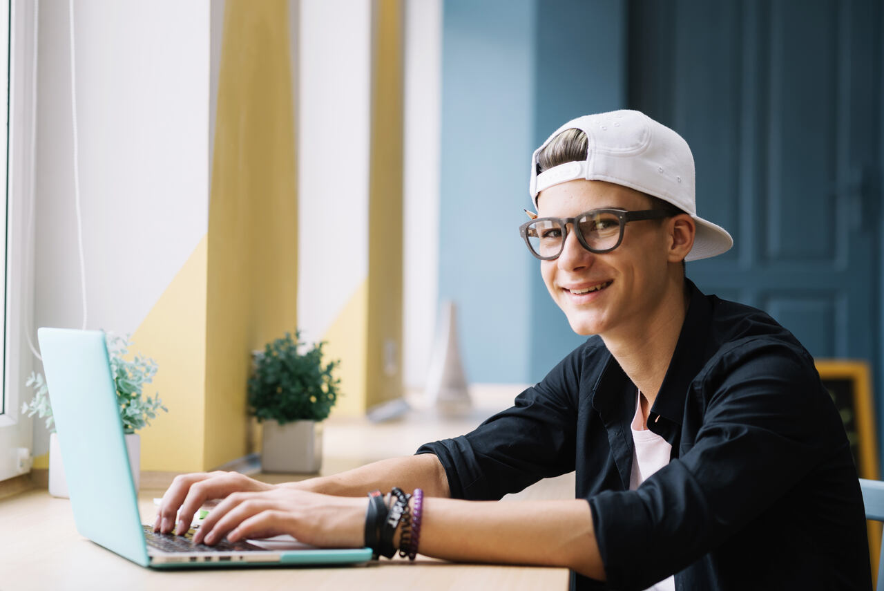 Adolescente posa sorrindo enquanto estuda em seu notebook 